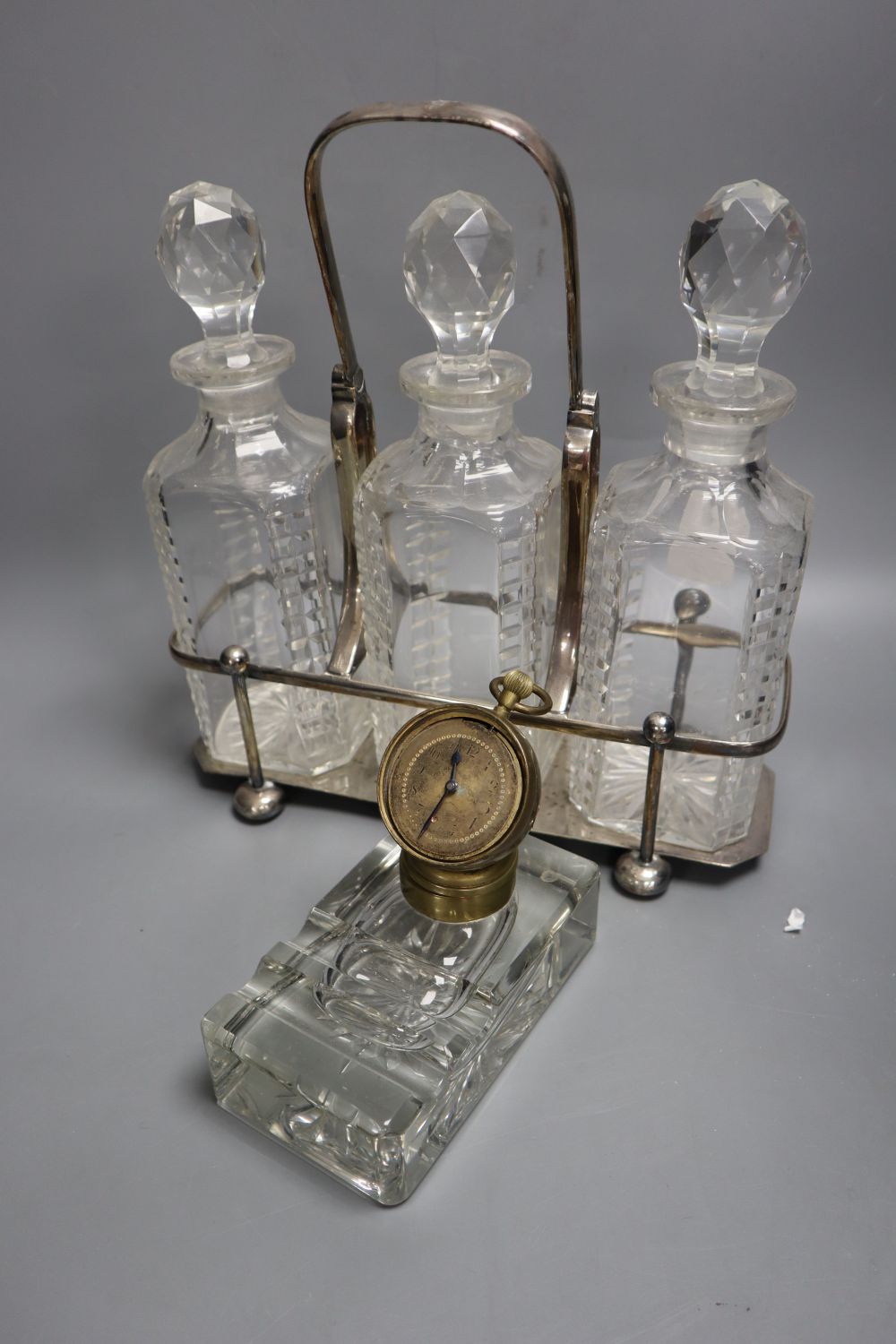 A late 19th century combination desk timepiece / inkwell, hinged timepiece on cut glass well, together with a three decanter tantalus